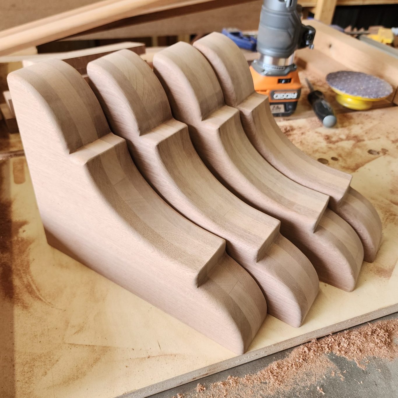 Several wooden corbels arranged side by side on a workbench beneath a router.