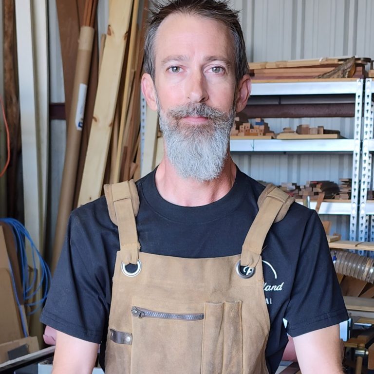 Kevin Pruitt wearing a work apron and standing in his woodworking studio.
