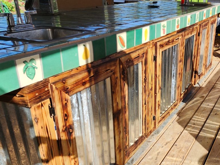Outdoor kitchen island with a Mexican tiled top and metal and shou sugi ban burned wood exterior.