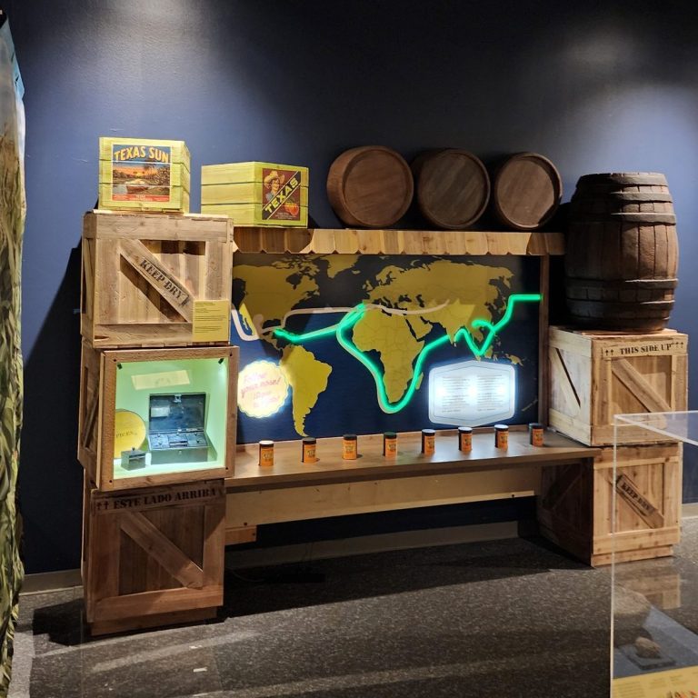 Museum display with a glowing world map, wooden crates, barrels, shelves, and spice cans.