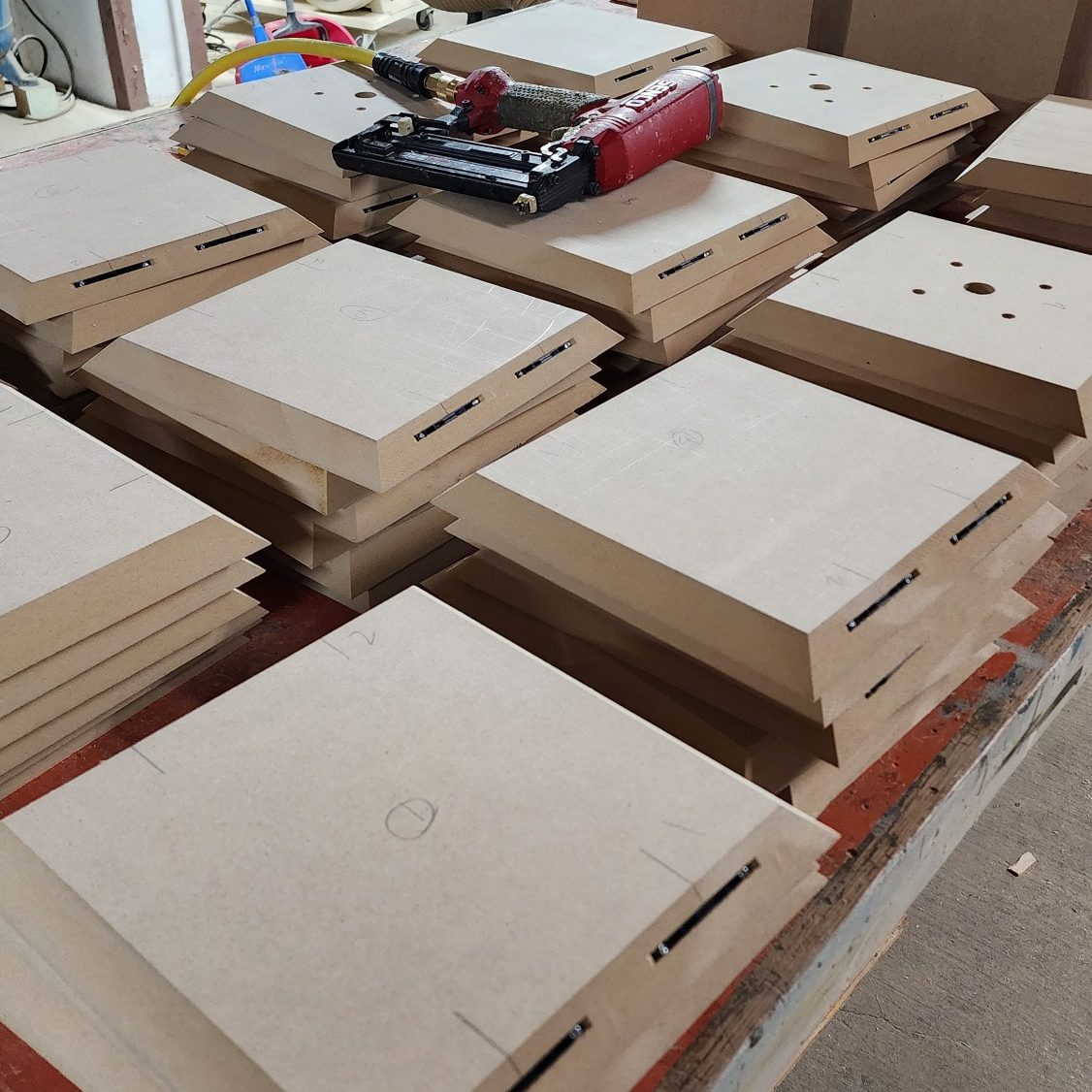 Light-colored square panels with routed slots and cutouts arranged across a work surface.
