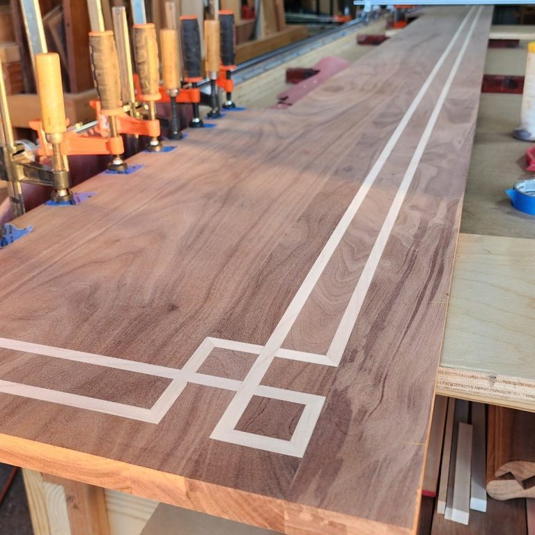 Long wood bar top with a geometric maple inlay pattern, shown in the workshop.