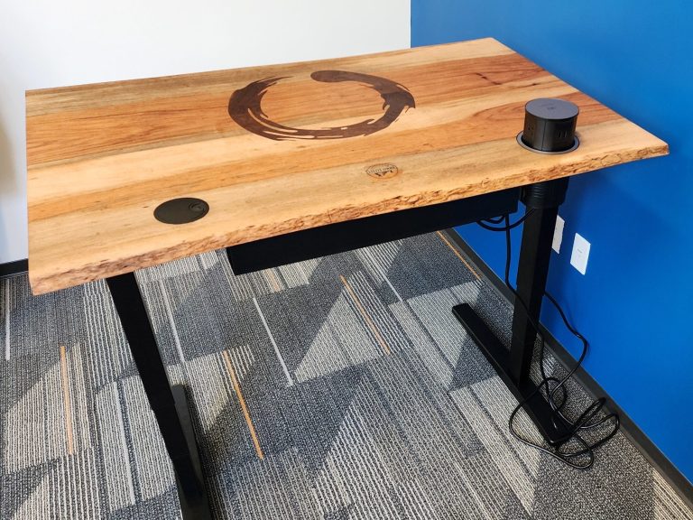 Wooden tabletop with inlay and electrical components, shown on a black sit stand desk.