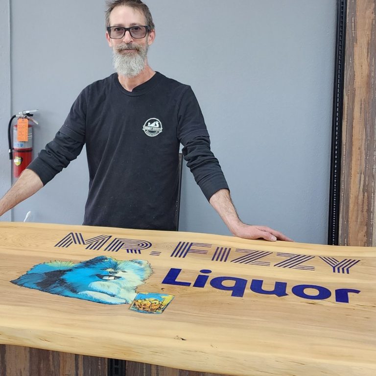 Kevin Pruitt standing behind a wood bar top with colorful lettering across its surface.
