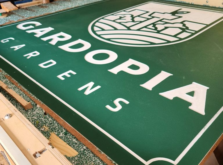 Green Gardopia Gardens sign panel on a CNC machine during fabrication.