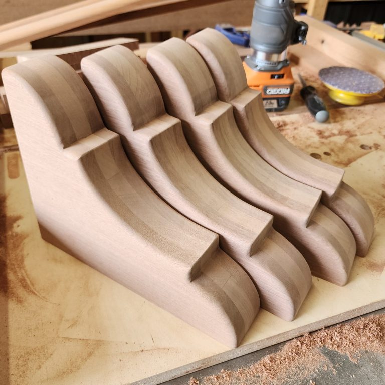 Custom wood corbels with shaped profiles arranged on a workbench.
