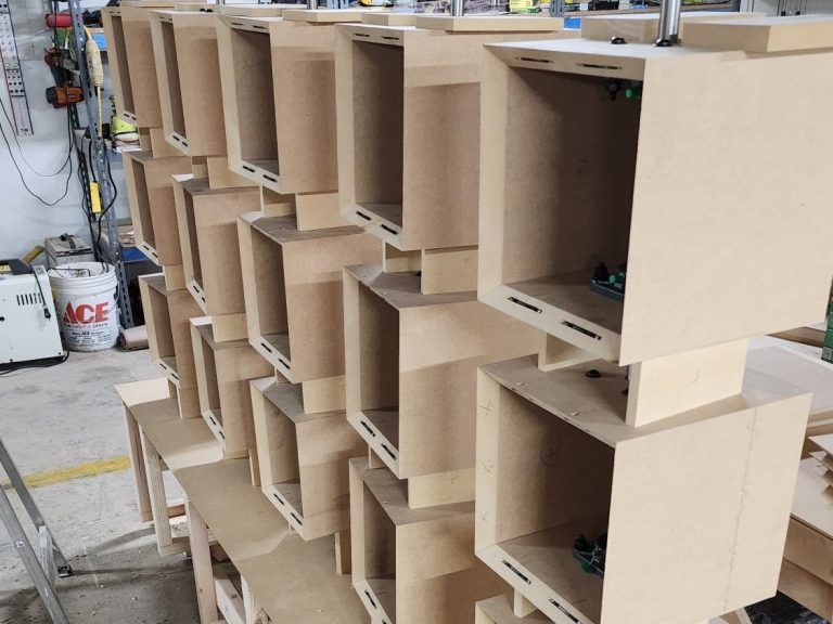 Flip Panel Cube Frames Rows of unfinished square cube frames arranged on shelving in the workshop.