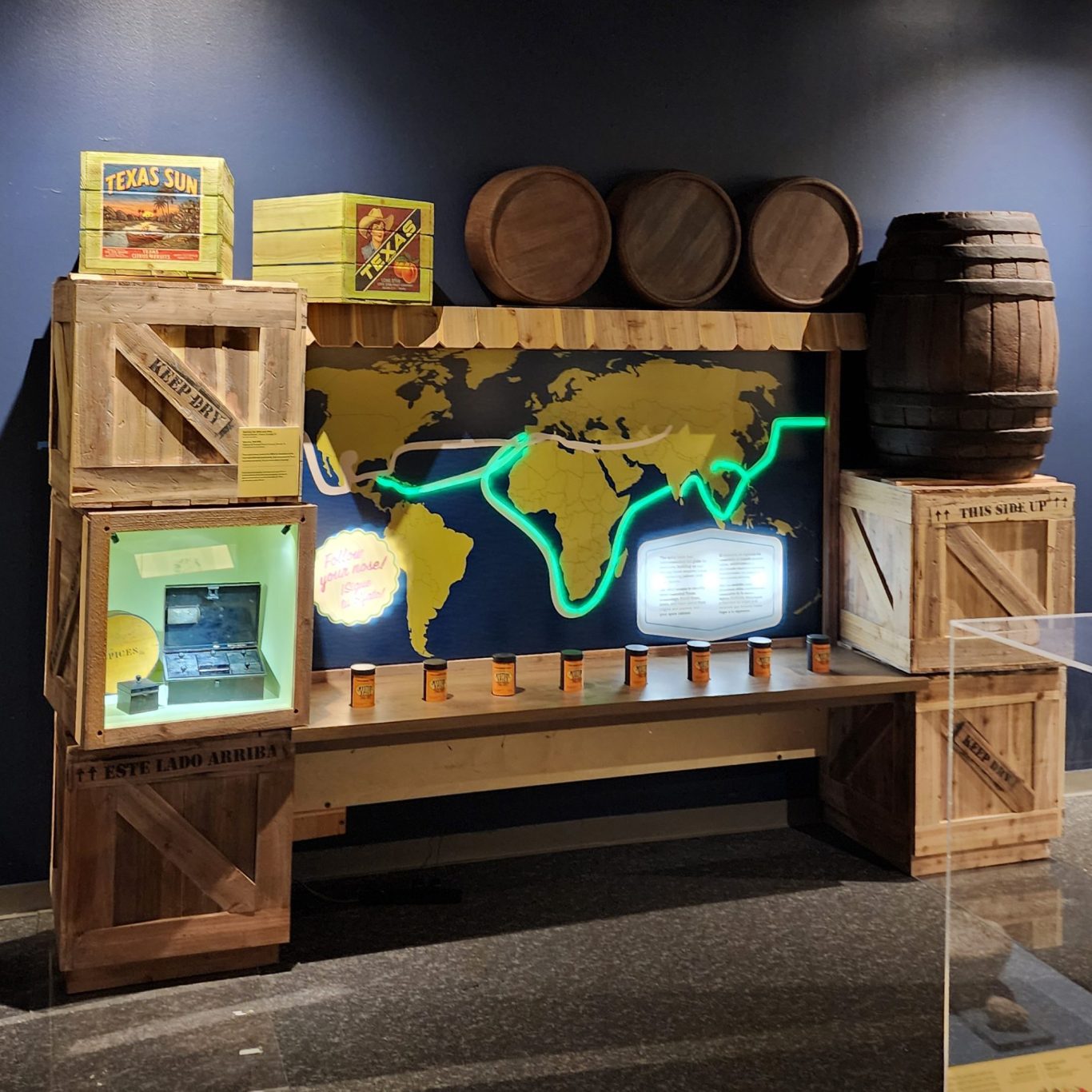 Museum display with a glowing world map, wooden crates, barrels, shelves, and spice cans.