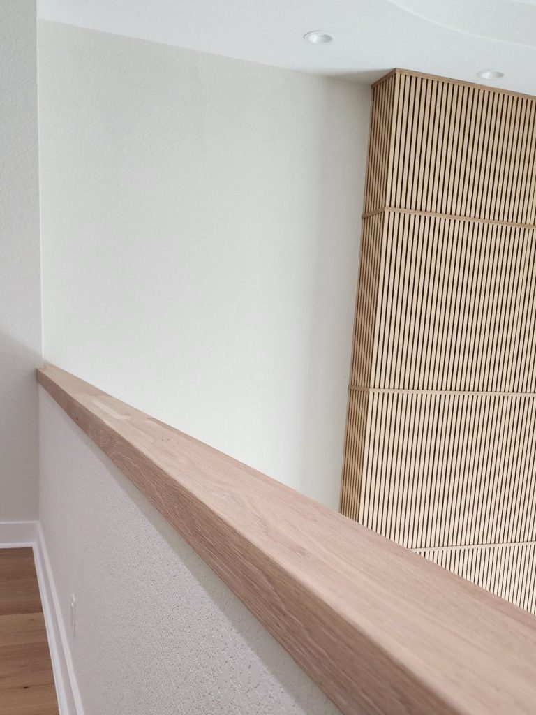 Wood rail beside a light interior wall with narrow vertical wood slats.
