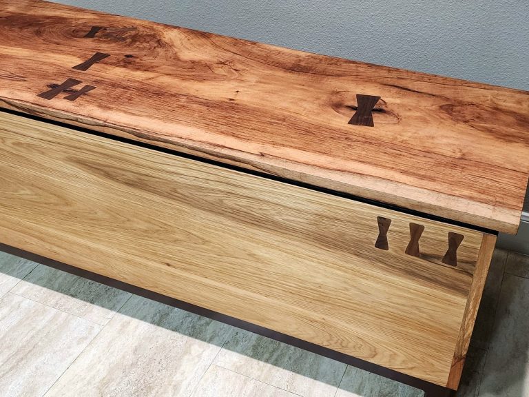 Pecan storage chest with dark colored metal frame and walnut bow-tie inlays across its surface.